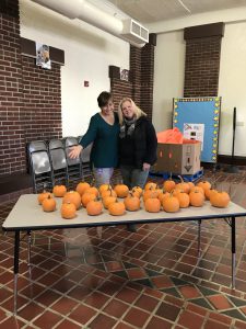 Two women standing near a table with pumpkins on it.