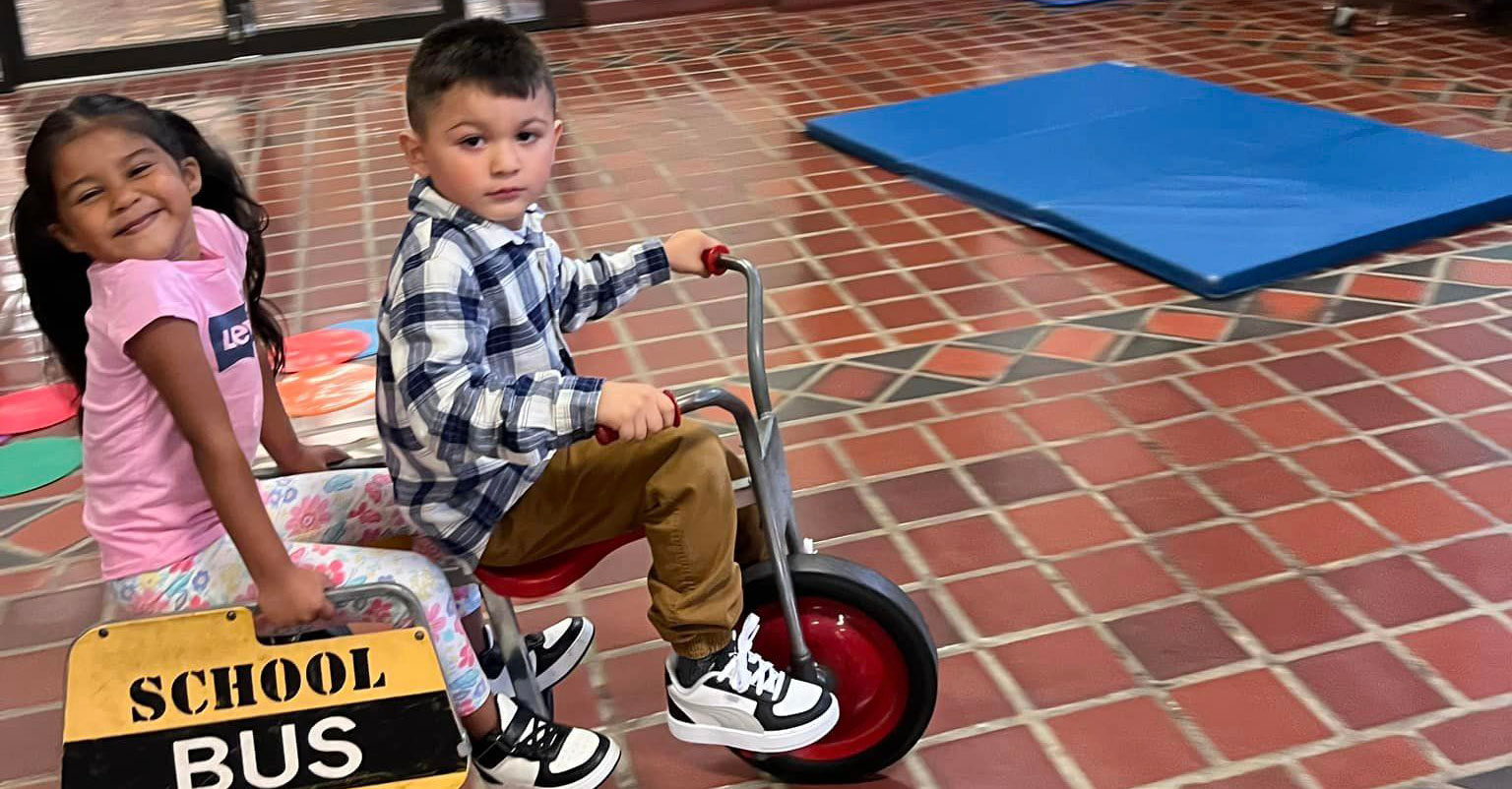 Two students riding a tricycle at school.