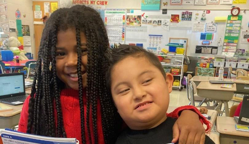 Two students holding notebooks smile for the camera with their arms around each other.