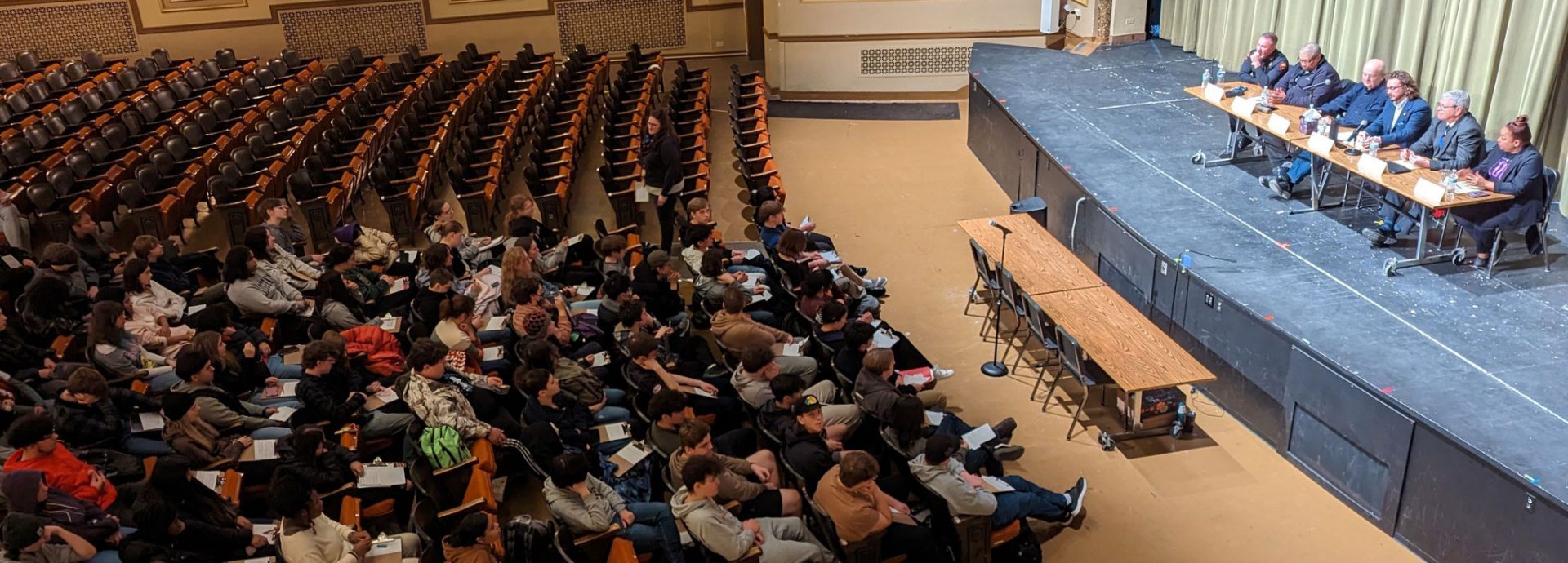 Birds eye view of students in the auditorium watching a panel discussion on stage.