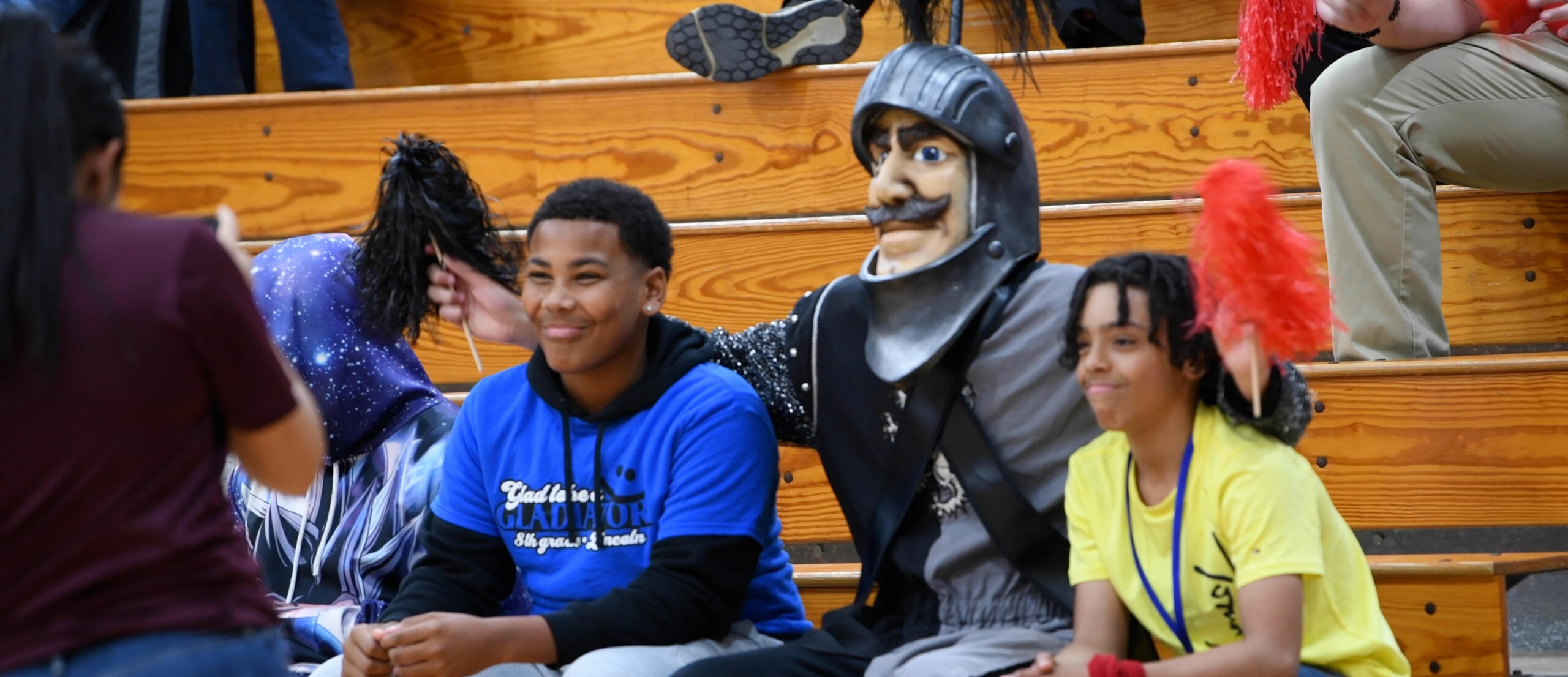 The Lincoln knight mascot sits with two boys on the bleachers.