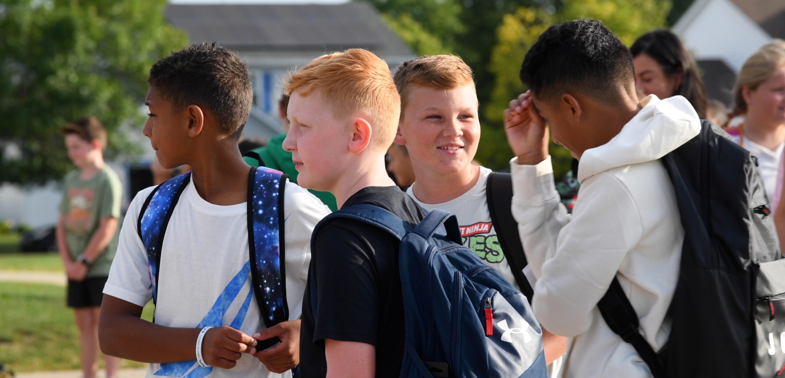 Four boys wearing backpacks and talking on the playground on the first day of school.