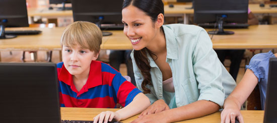 A teacher working with a boy at a computer.