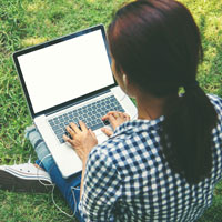 A student sitting in the grass, using a laptop