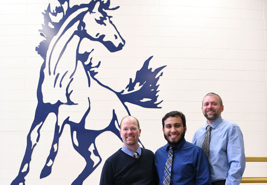 Mr. Landgraf, Mr. Hernandez, and Mr. Bishop standing in front of the old Mahone mustang logo on the wall.