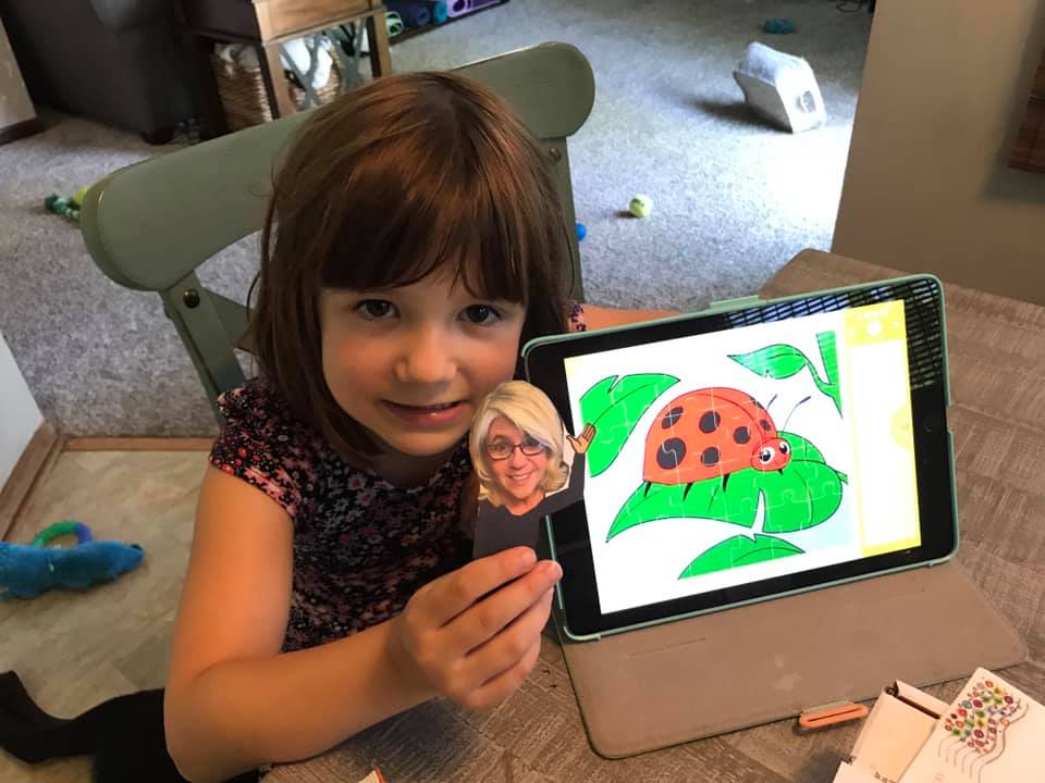 A student holding "flat Beth" next to an iPad with a ladybug on the screen.