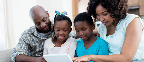 A mother and father use a tablet with their daughter and son.