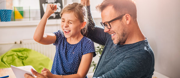 A father and daughter raising their hand in excitement while playing something on a tablet.