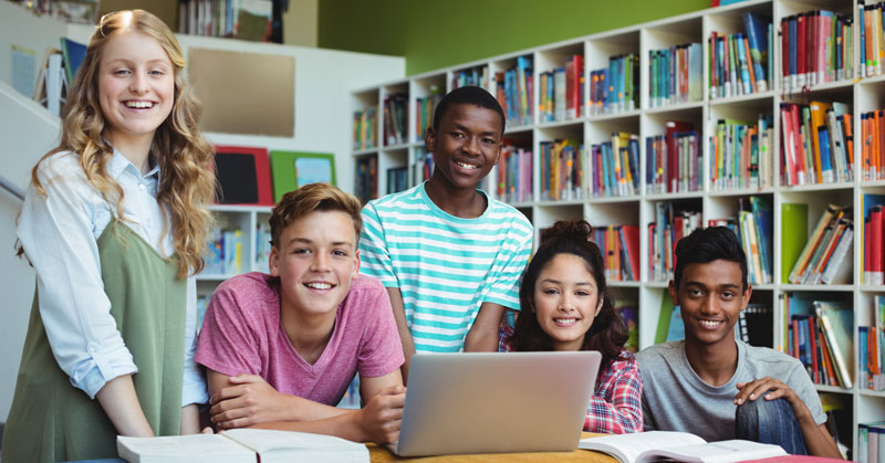 five students in the library with a laptop and books