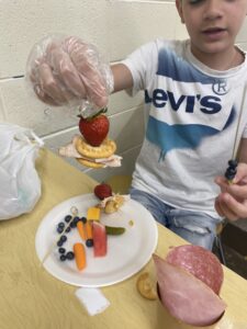 A student wearing a white Levi's shirt lifts up a charcuterie he is working on.