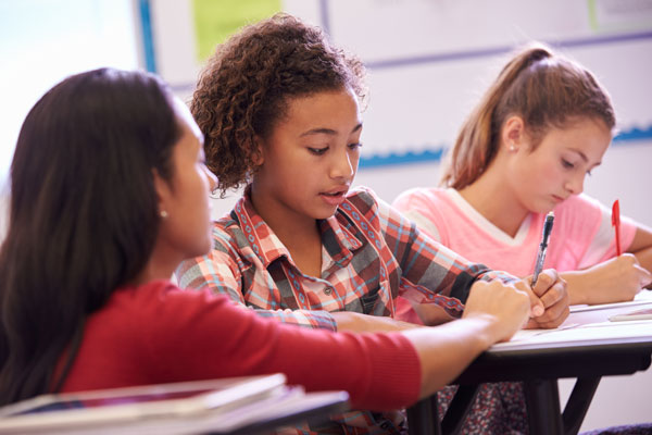 A fifth grade girl getting help from a teacher at a desk.