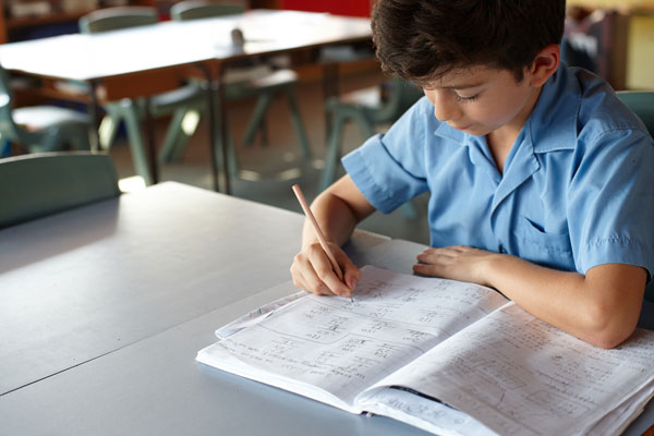 A fourth grade boy sitting at a table, writing in a workbook.