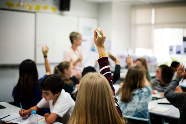 Students raising their hands in a classroom.