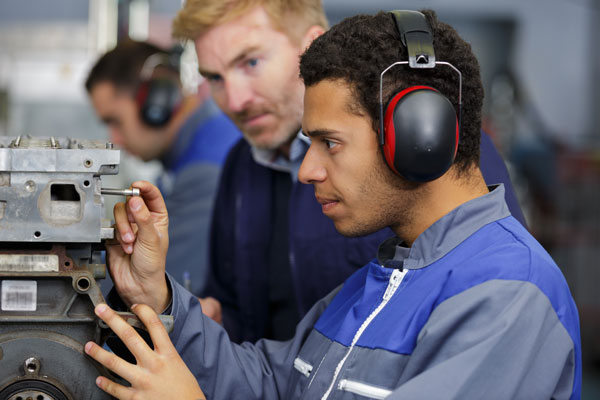 A student wearing protective headphones works on some machinery.