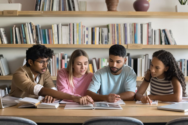 Four students sitting at a table looking at a book.