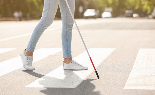 Bottom half of a person using a cane, walking in a crosswalk