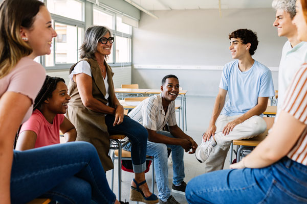 A group of high school student talking to a teacher in the classroom.