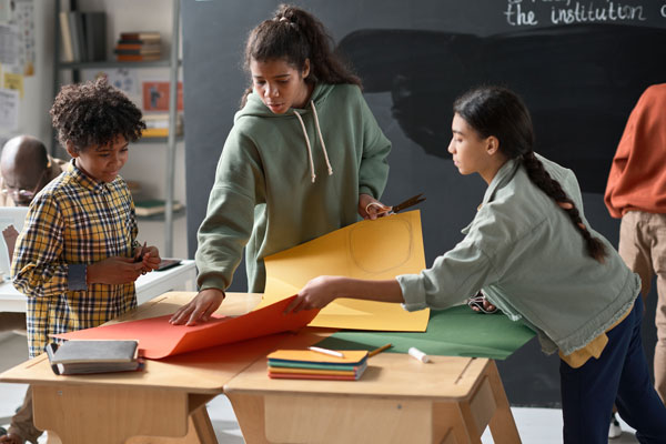 Group of children making craft work from colorful papers together during lesson in the classroom
