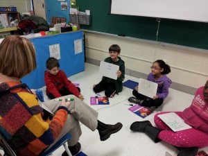 Four students sitting on the floor in front of their teacher.